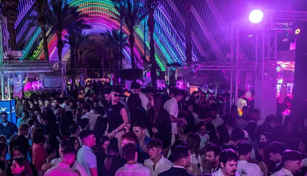 Large crowd partying on an open-air terrace with purple lights and palm trees in Valencia.