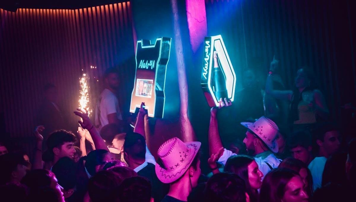 Party crowd raising hands under neon lights during a club night in Valencia.