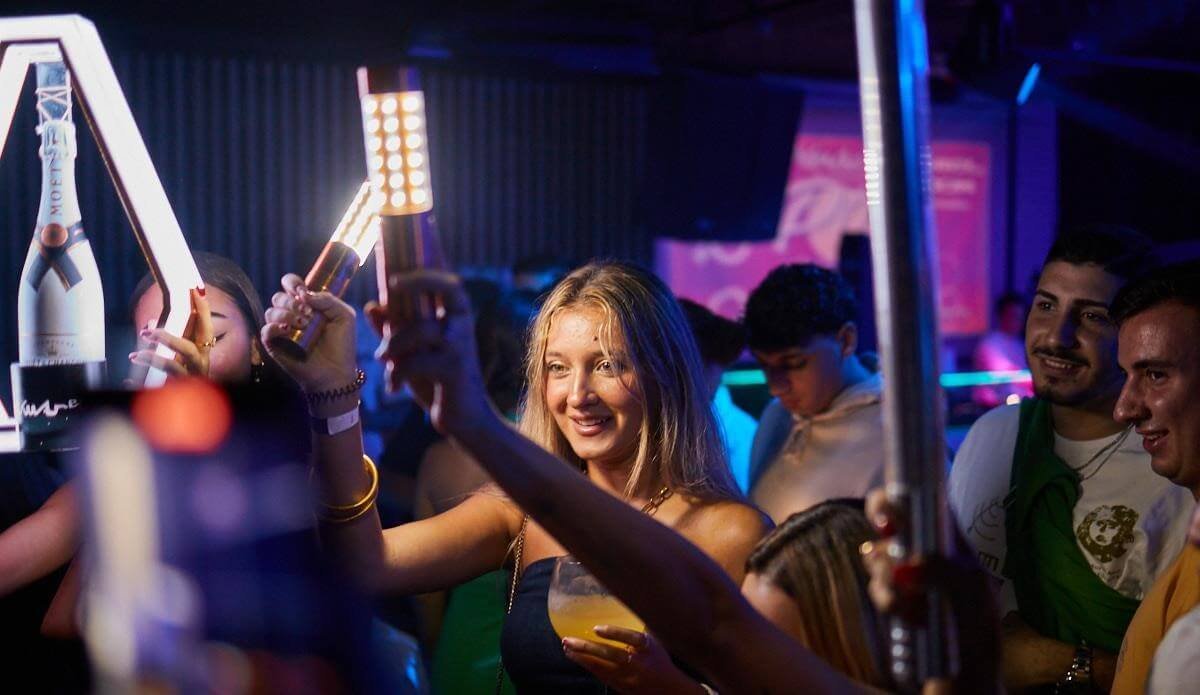 Woman raising her phone while dancing in a nightclub crowd in Valencia.