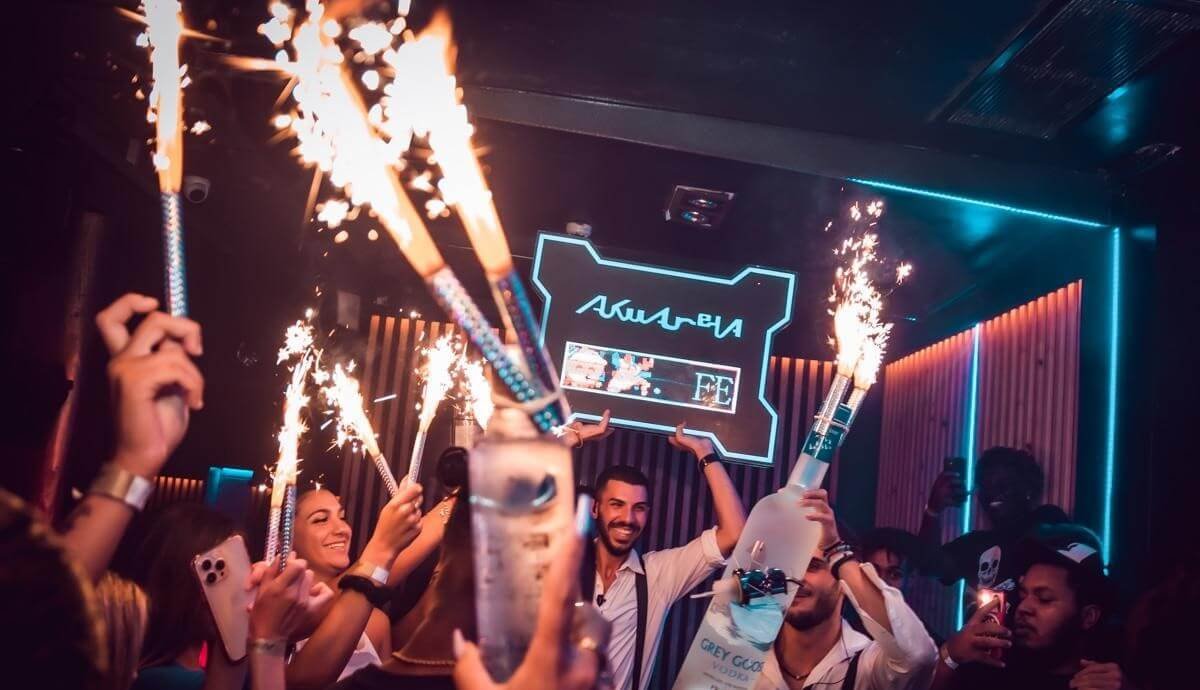 Party crowd holding sparklers and bottles at a beach club night in Valencia.