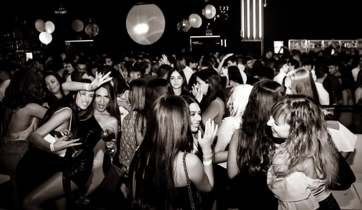 Black-and-white nightclub crowd socializing on the dancefloor.