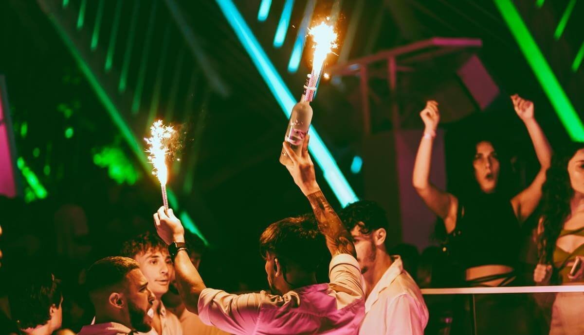 Guests celebrating with sparklers and bottles during a nightclub party at night.