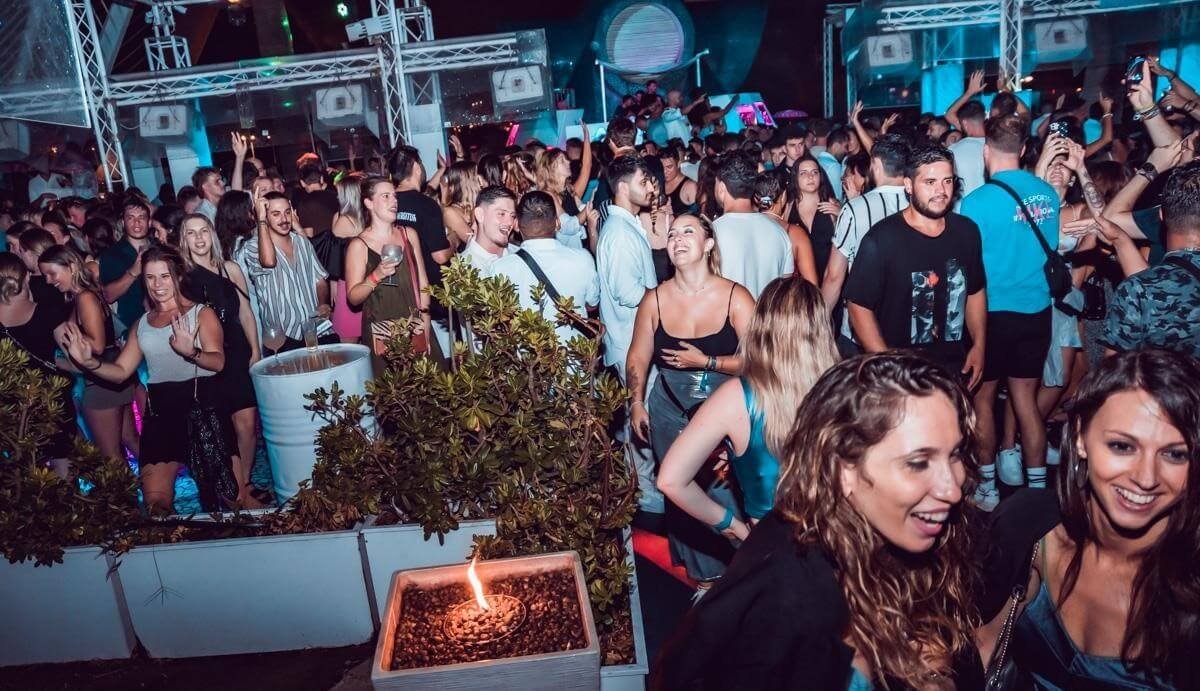 People socializing at an open-air club area with terrace lighting at night.